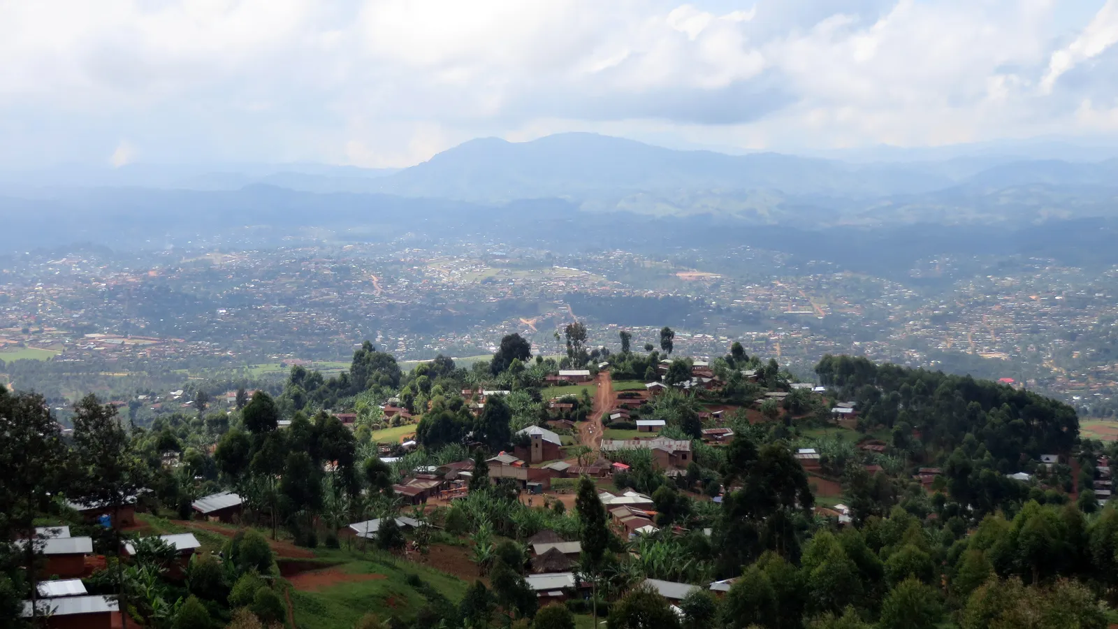 Green hills covered with houses and trees above Butembo in North Kivu, with blue mountains in the distance