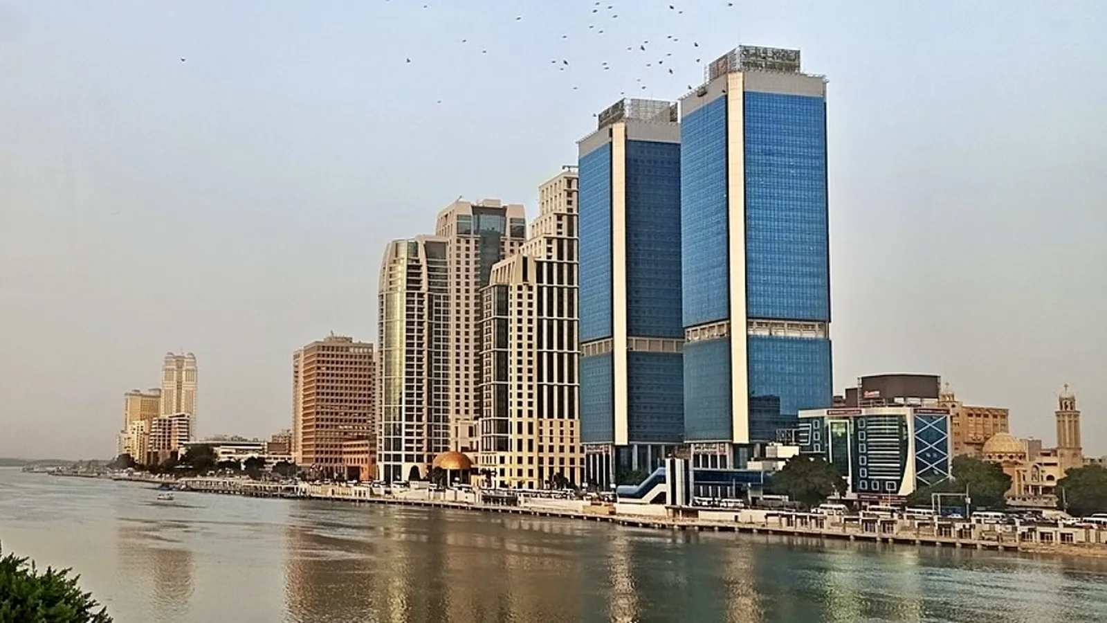 Office towers along the Nile Corniche in Cairo, reflected in the river under a pale sky