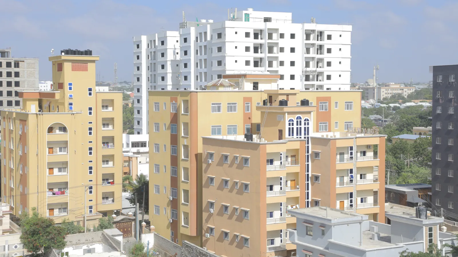 Newly built cream and orange apartment blocks and a white high-rise against a blue sky in uptown Mogadishu