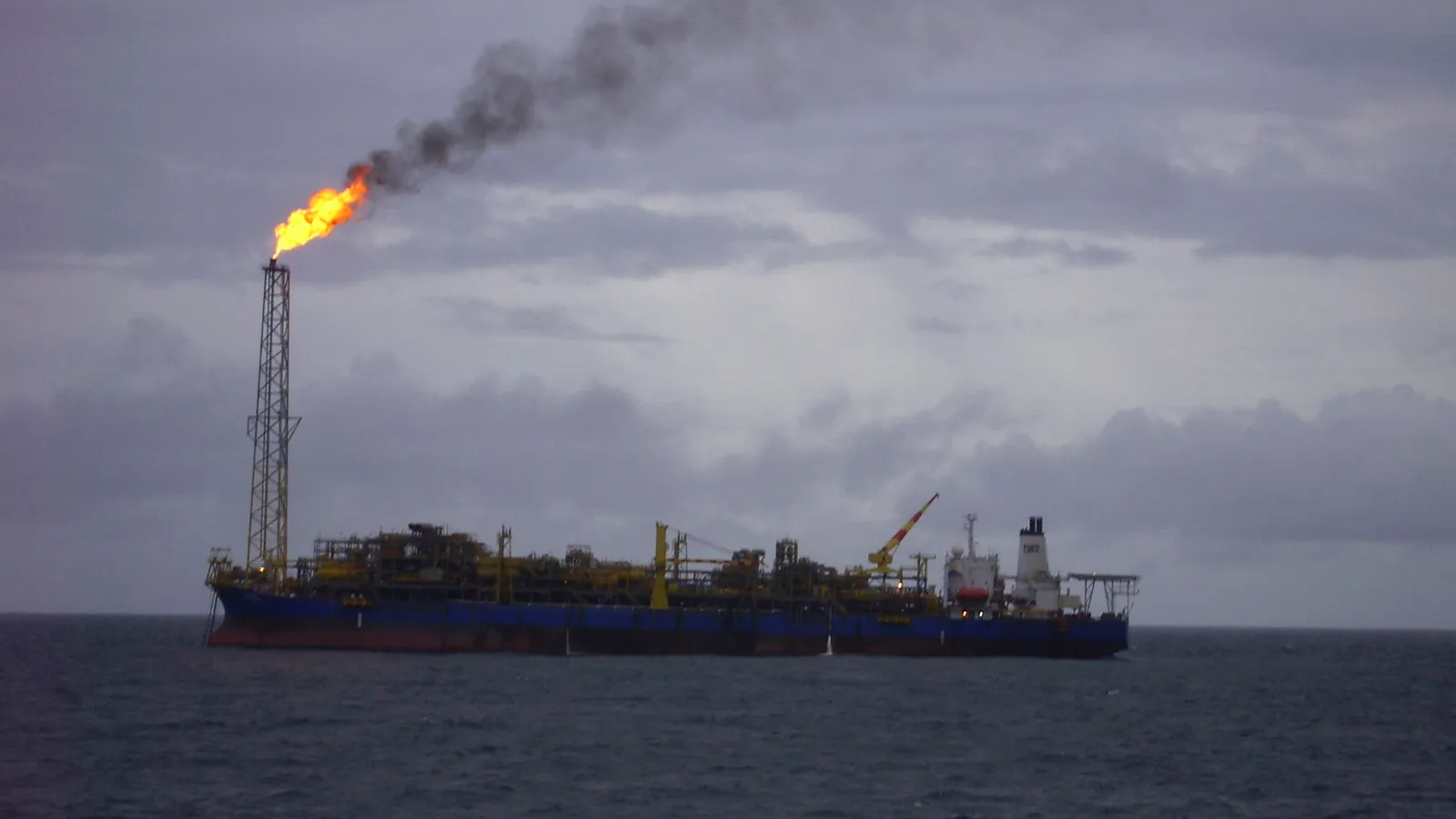 A floating oil production vessel with a burning gas flare on the open sea off Nigeria under grey cloud